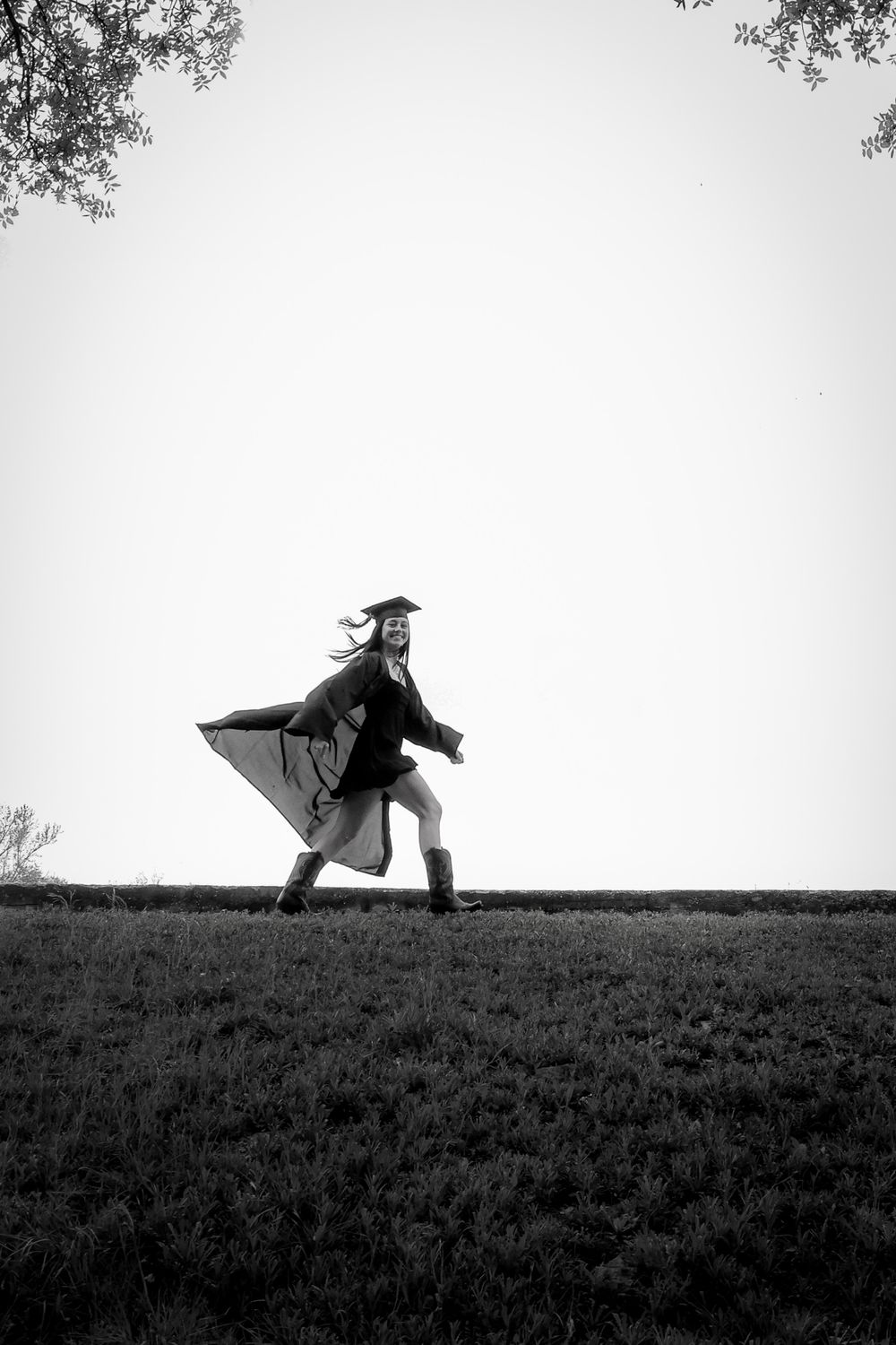 A silhouette of a graduate running joyfully on a hilltop in black and white.