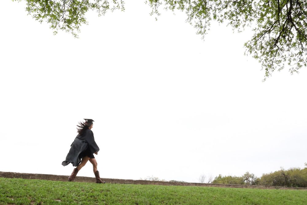 A silhouetted graduate walking across a hilltop against a bright sky.