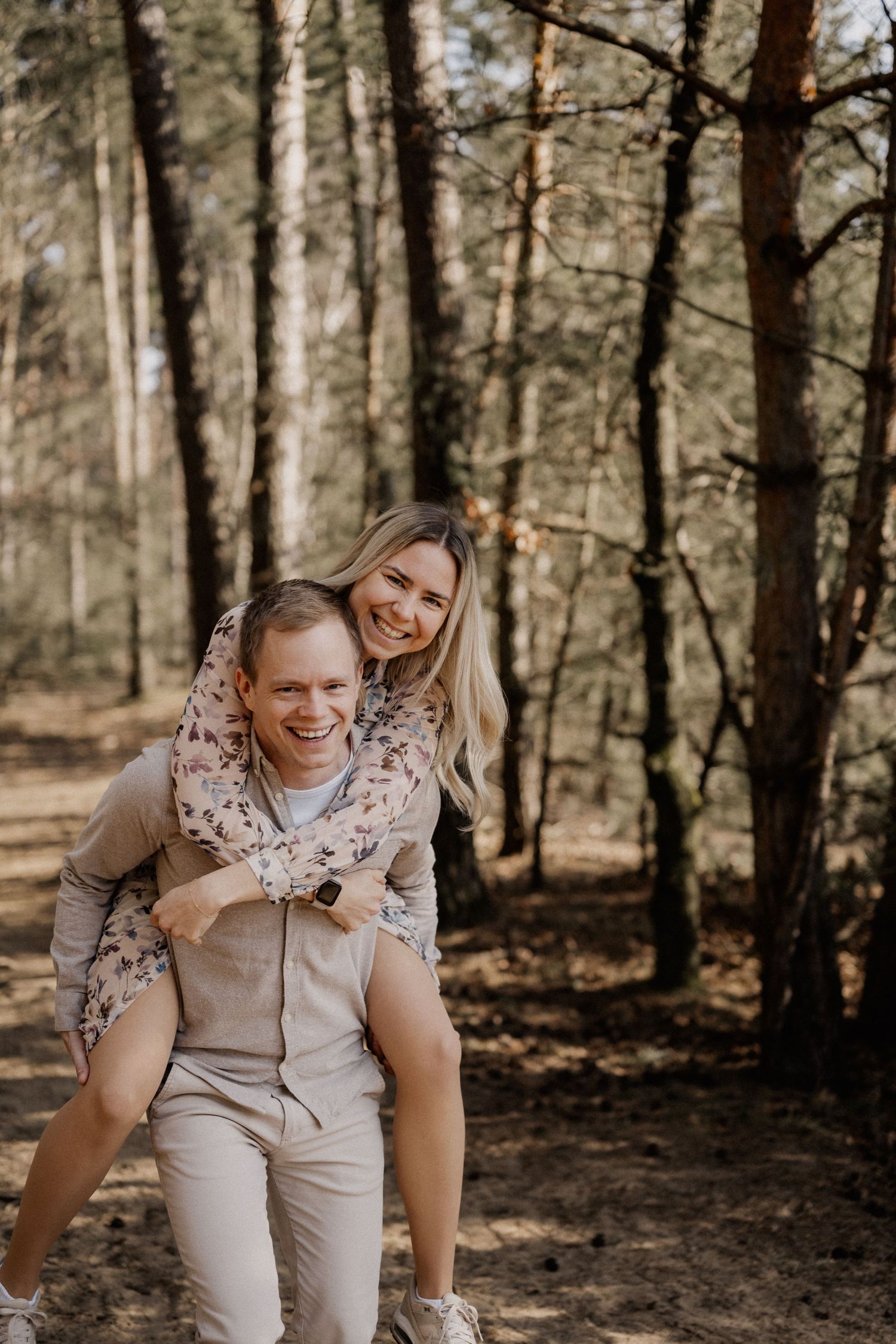 A couple enjoying a piggyback ride while exploring a scenic forest path on a sunny day.