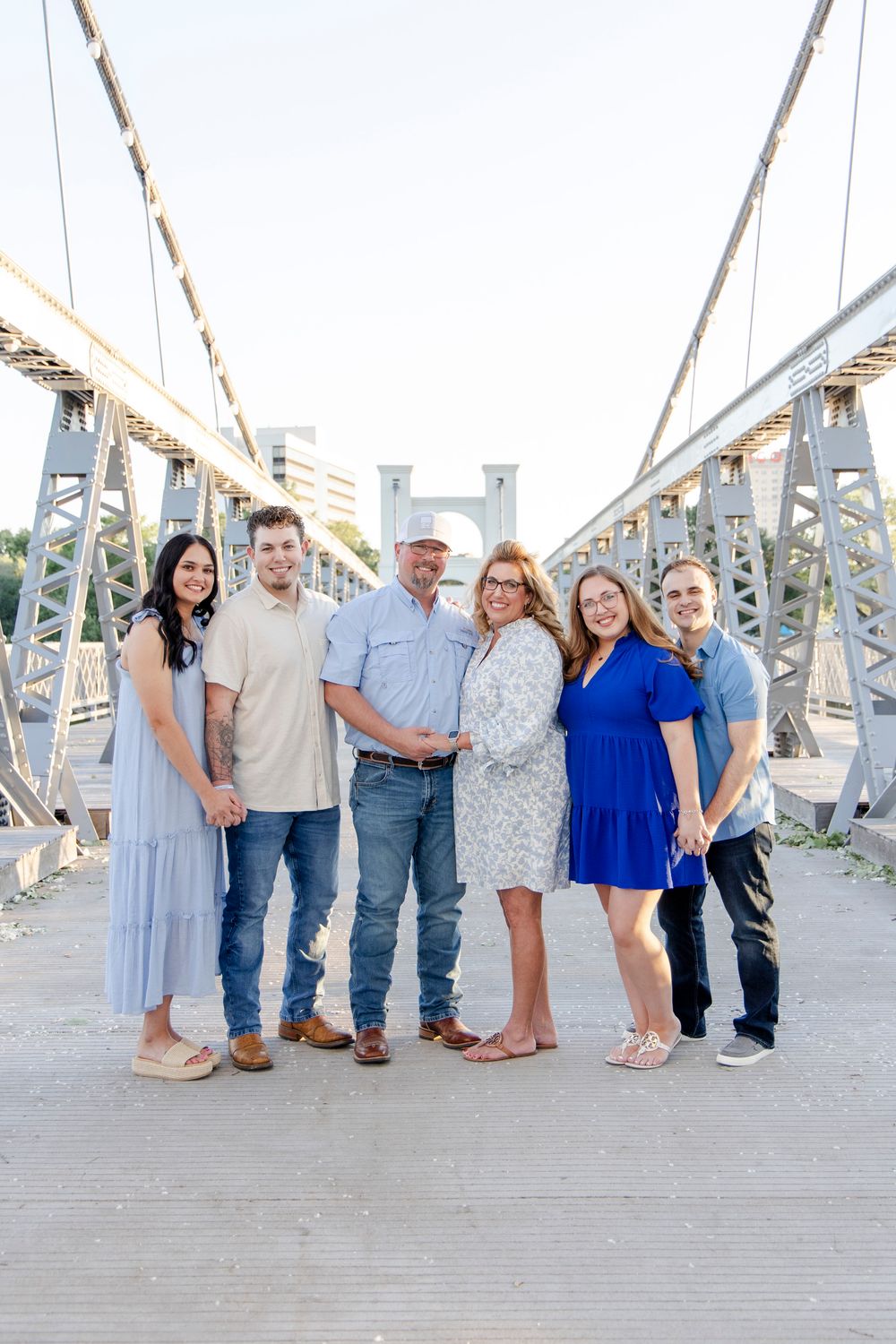 A group of six people pose together on a metal bridge structure on a bright sunny day.