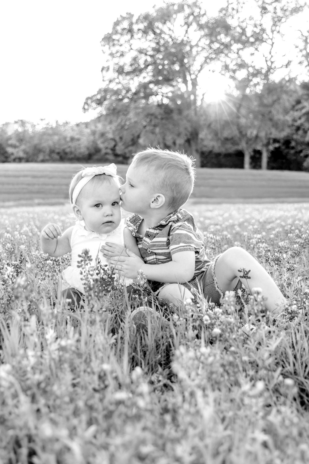 Sweet black and white portrait of two small children sitting together in a sunny wildflower meadow.