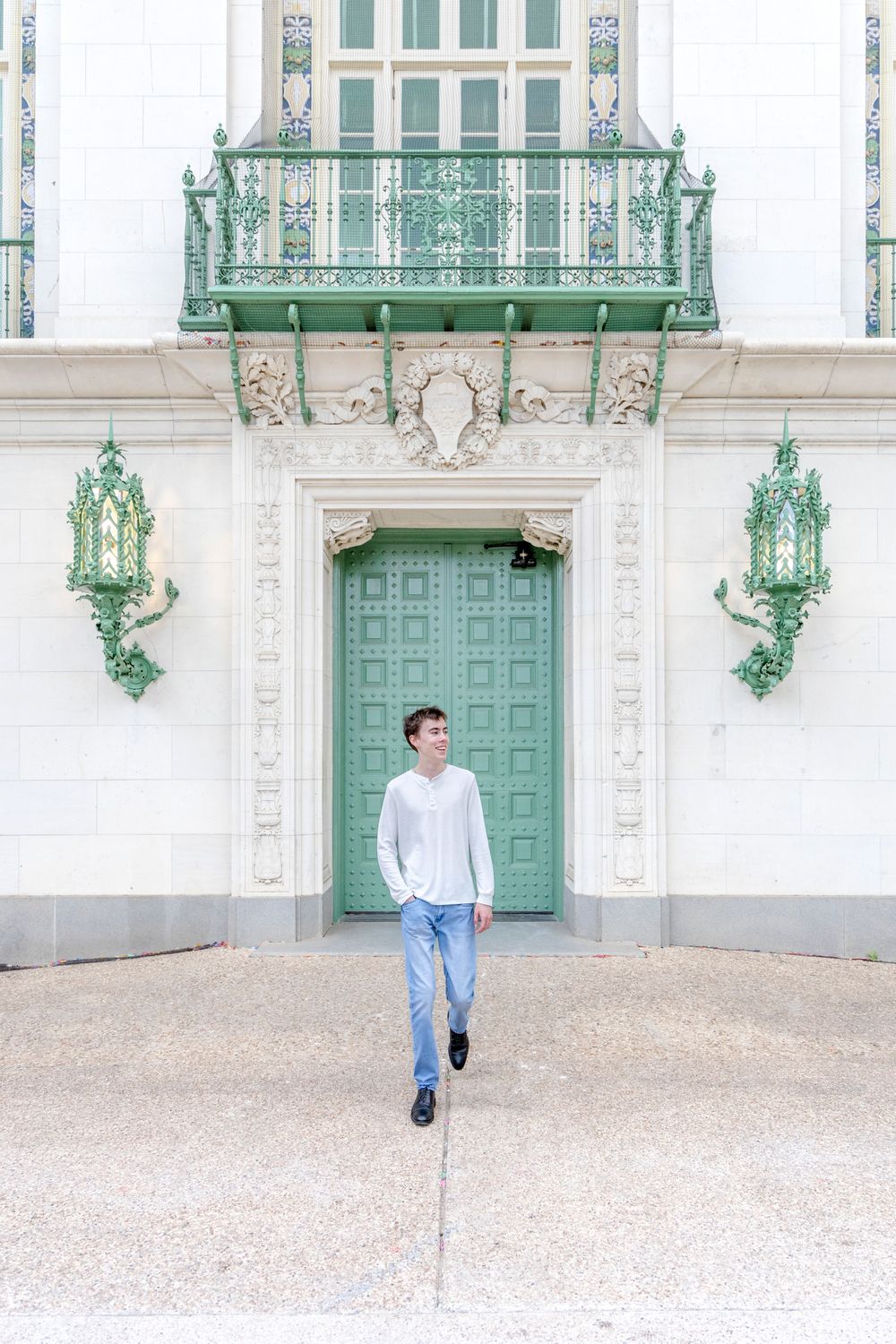 A person in a white shirt and jeans stands in front of an ornate mint green door with decorative metalwork above.
