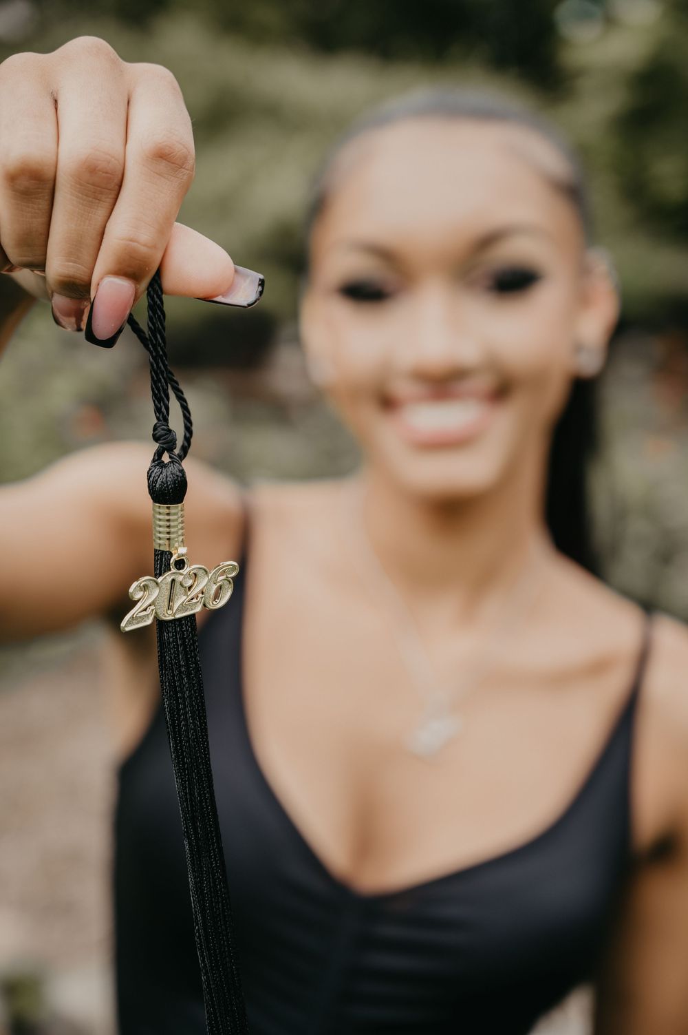 Smiling graduate holds up a black tassel with gold 2026 charm for senior portrait photo.