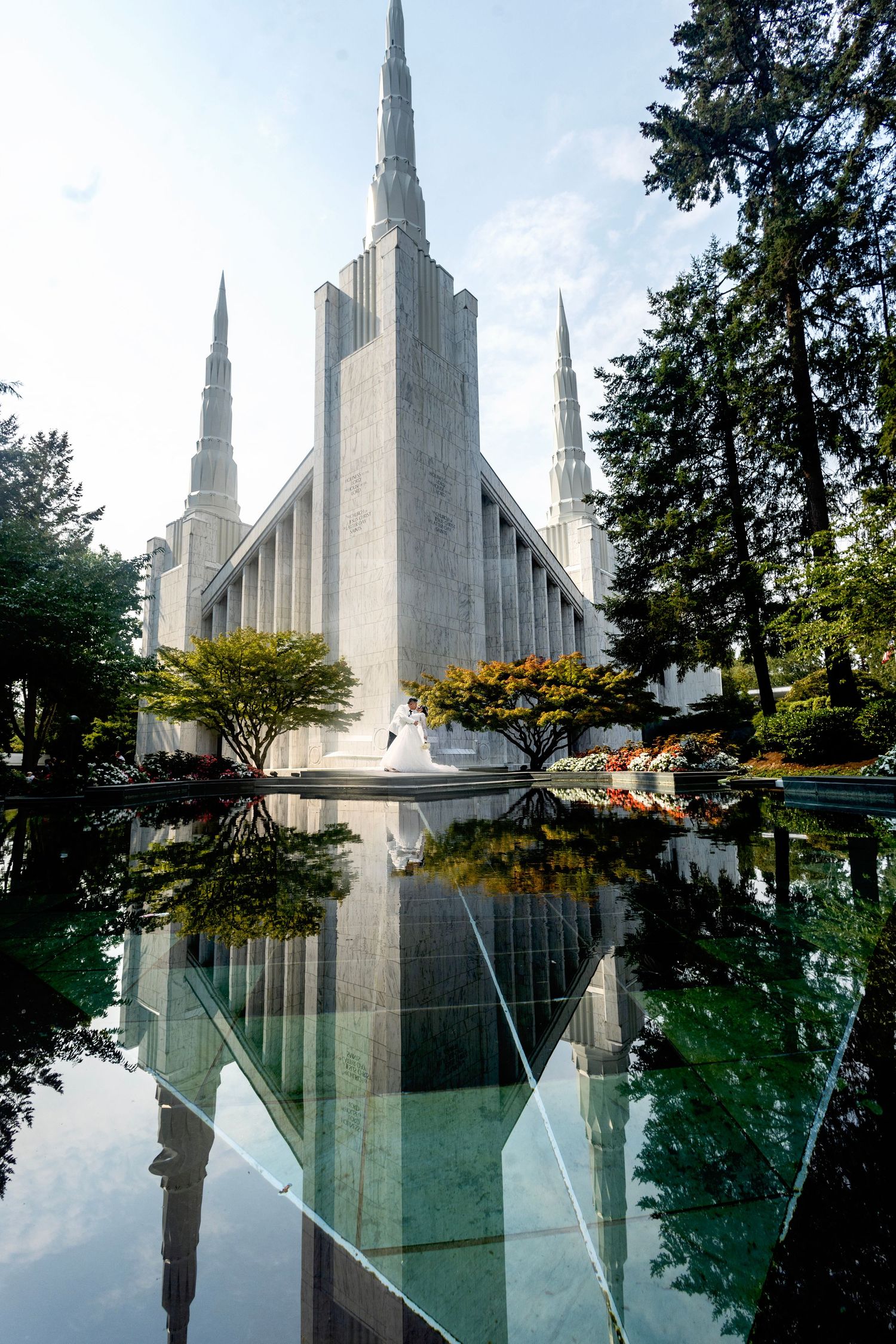 Mormon temple reflected in still water with trees framing the symmetrical architecture.