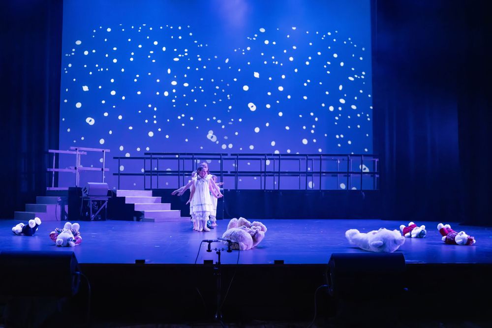 Solo performer stands center stage while others lay down during nighttime scene with starry backdrop.