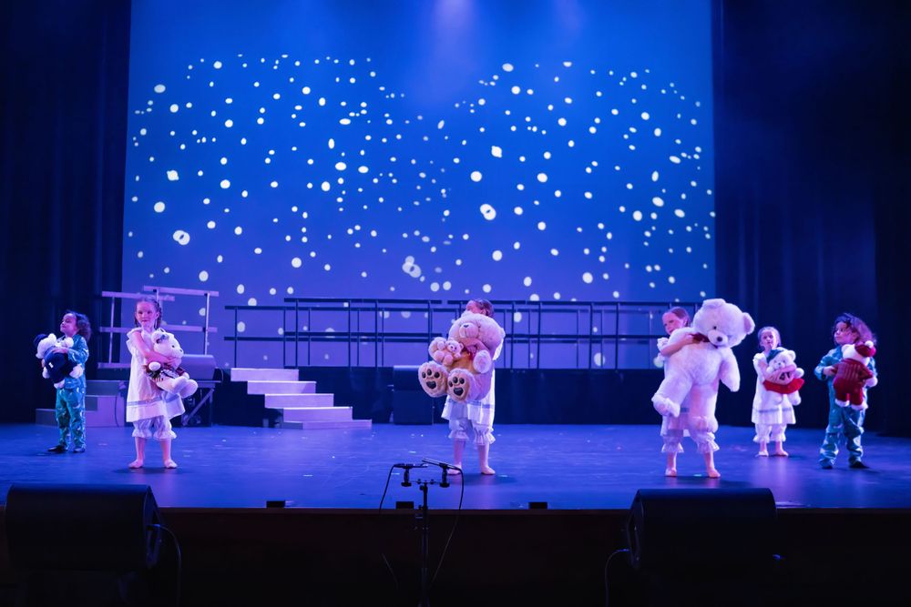 Performers in costume arrange themselves across a stage with twinkling star effect backdrop.