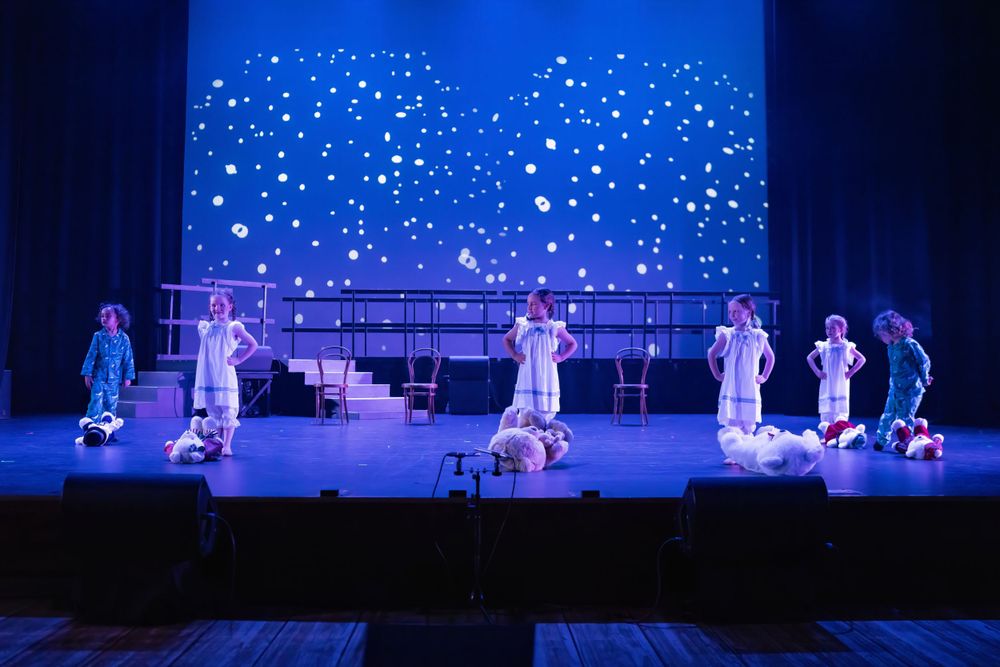 Dancers perform under a starlit backdrop on a multi-level stage set with blue lighting.