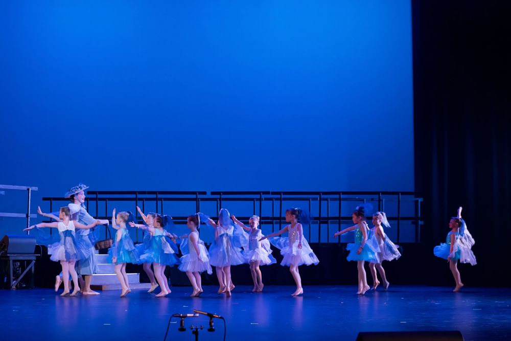 Dance ensemble performs graceful movements in matching blue and white costumes on an illuminated stage.