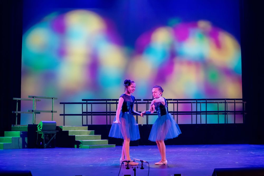 Two dancers in blue costumes perform a duet against a multicolored backdrop.