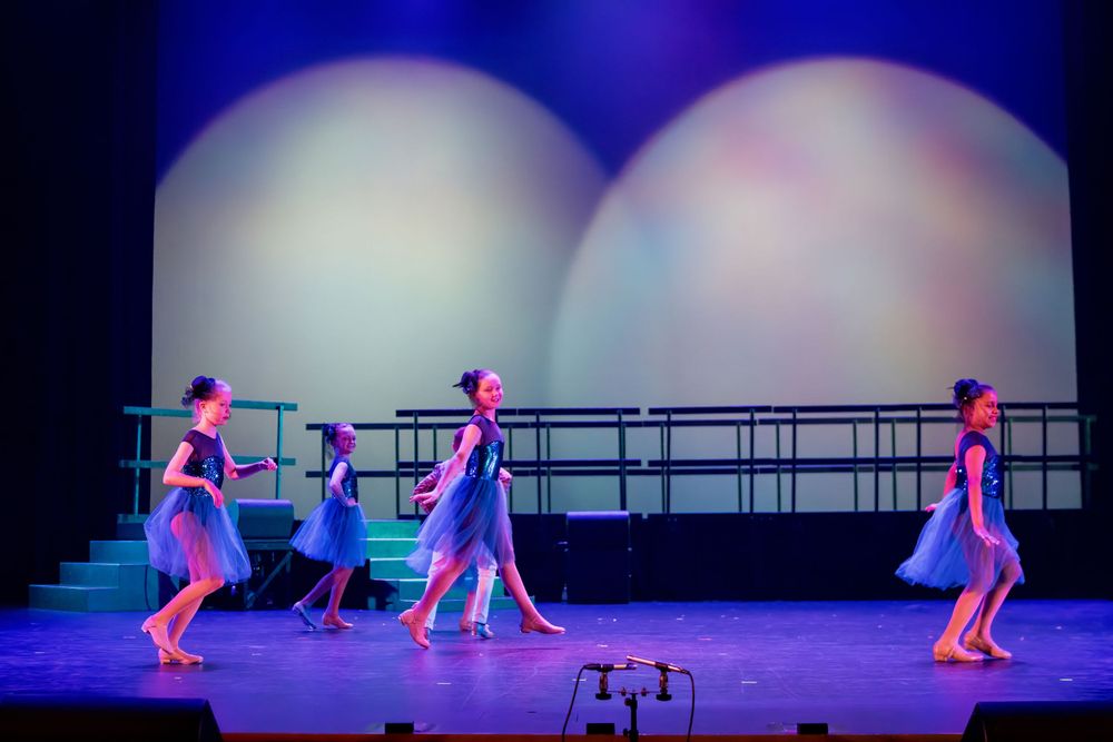 Dancers in blue costumes perform against circular lighting effects on a darkened stage.