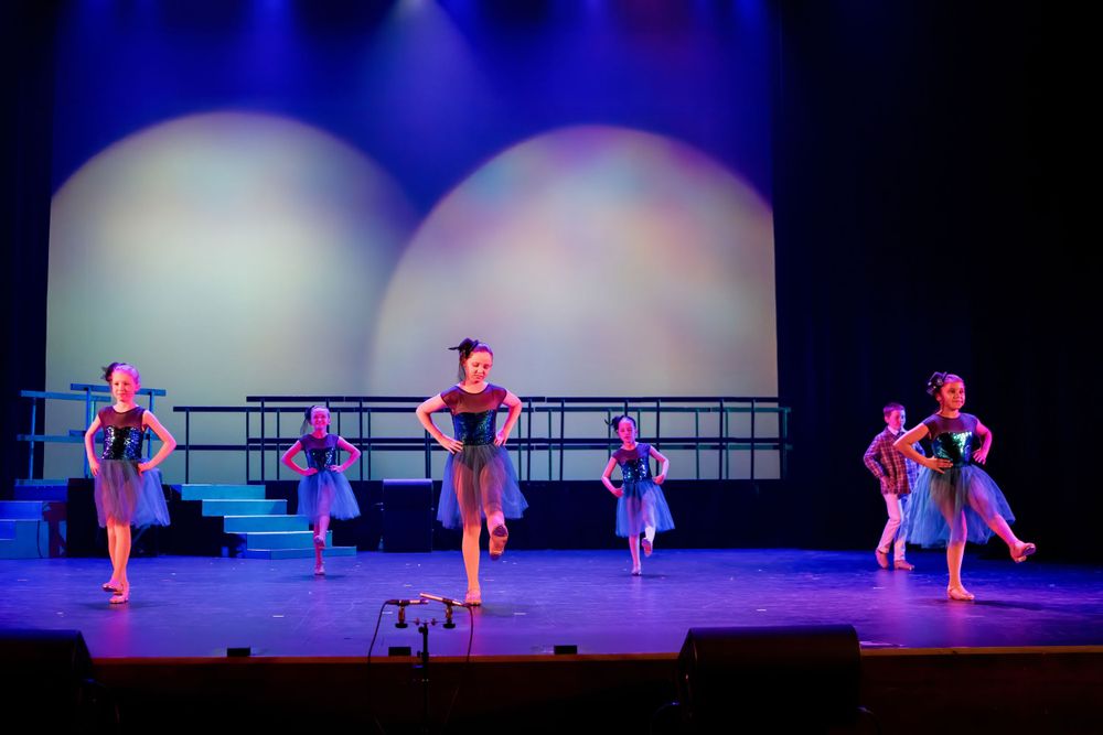 Dance recital with performers in coordinated blue outfits under dramatic stage lighting.