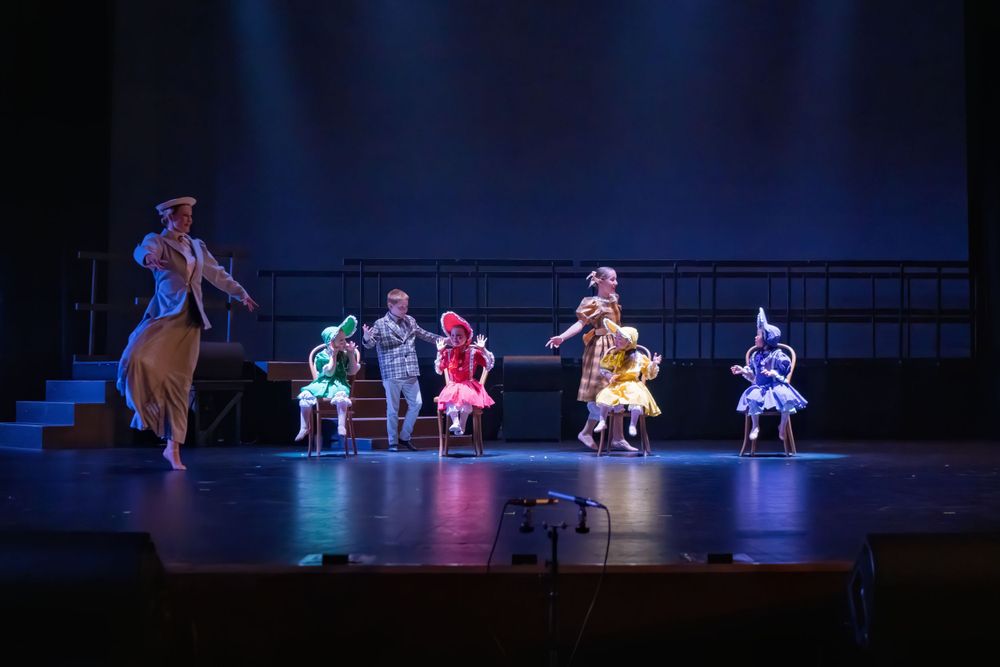 Theater performers in vintage costumes dance across a staged platform during a musical production.