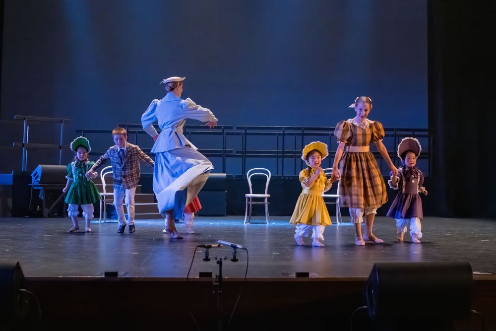 Dancers in bright period costumes perform an energetic choreographed routine on stage.