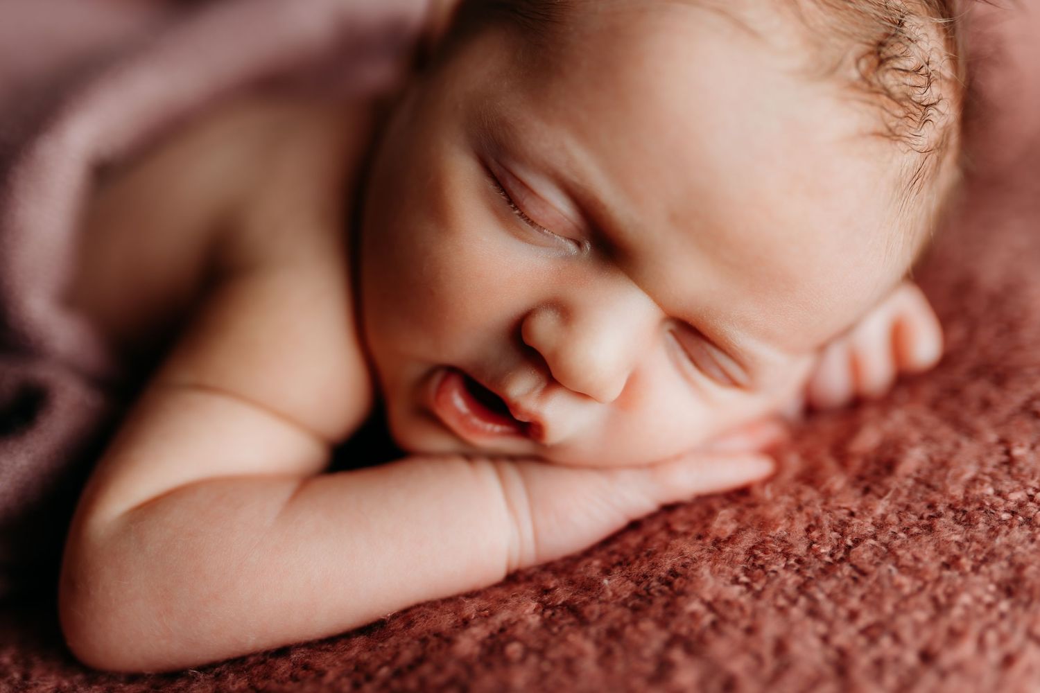 Close-up of sleeping newborn baby on soft pink textured fabric.