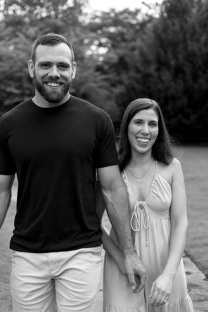 Black and white. A couple is holding hands and smiling at the camera.