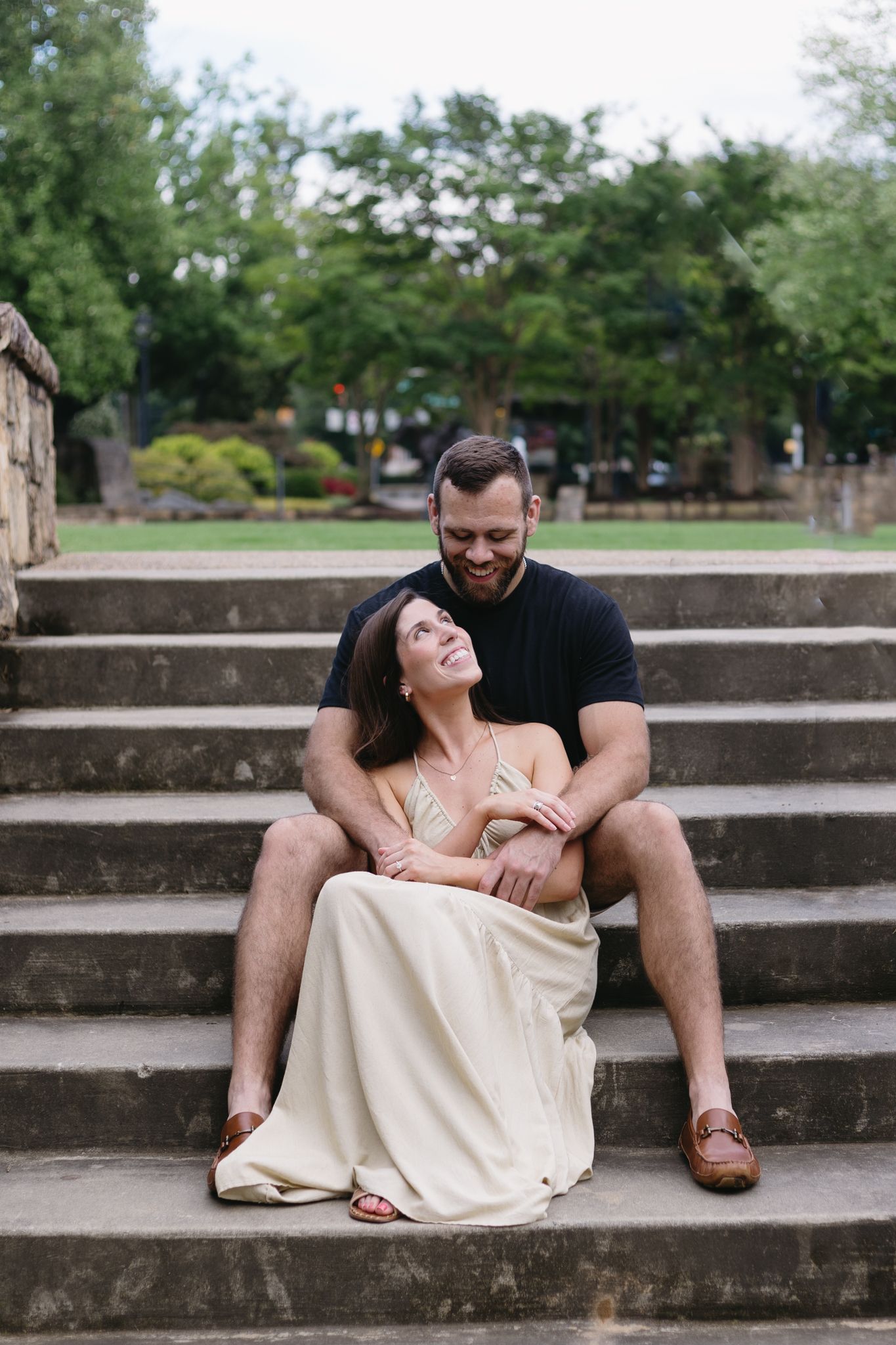 A man holds his fiancé as she sits between his legs on the steps of downtown Charlotte.