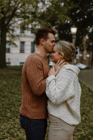 A man lovingly kisses his fiancé on the forehead.