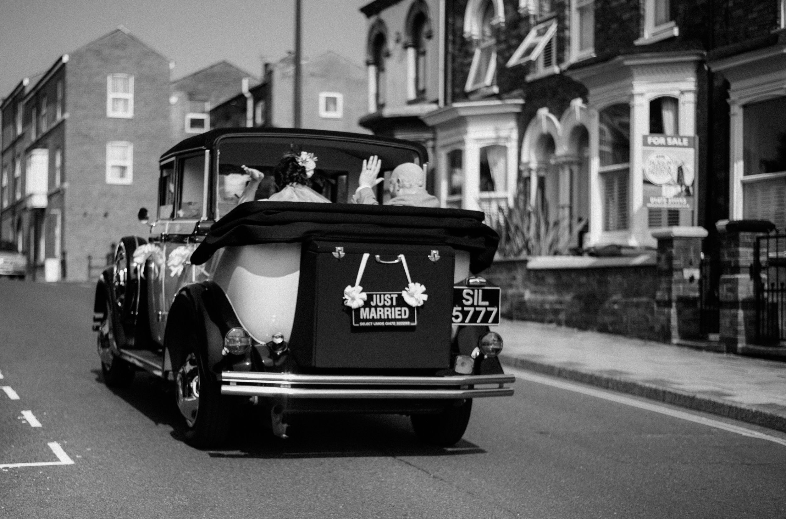 Black and white photo of vintage wedding car driving down a residential street.