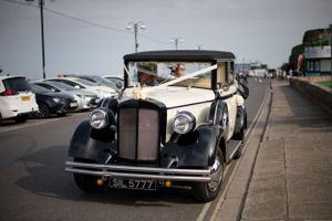 Vintage cream-colored wedding car parked in seaside lot.
