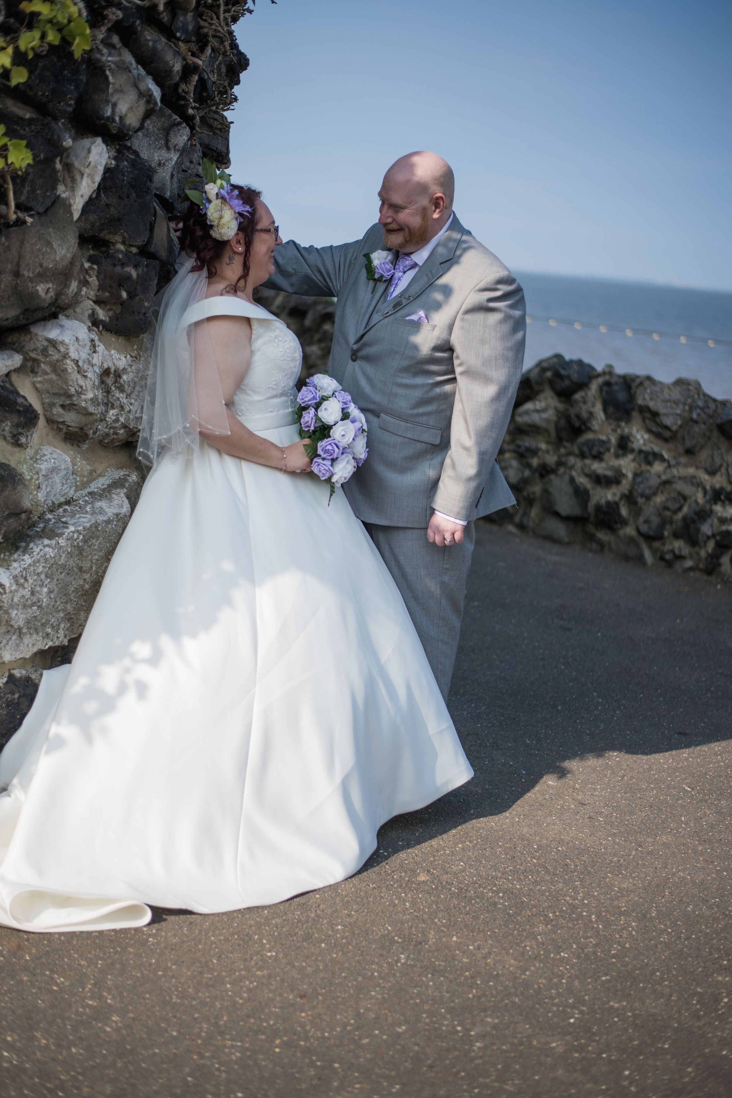 Newlyweds share a romantic moment against rocky coastal backdrop with ocean view.