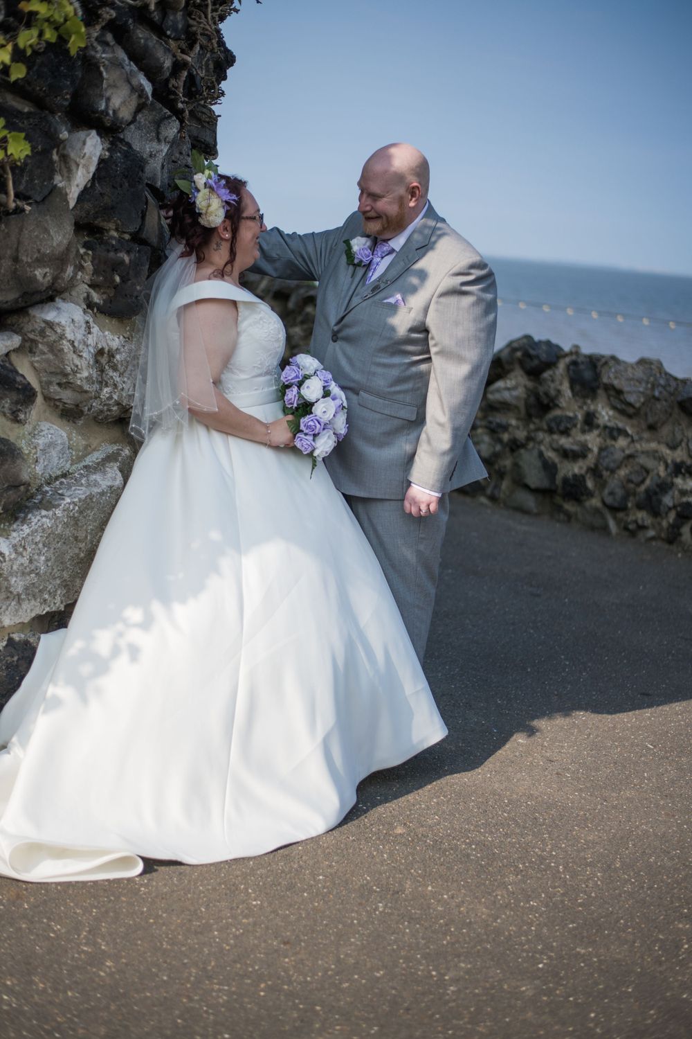 Newlyweds share a romantic moment against rocky coastal backdrop with ocean view.