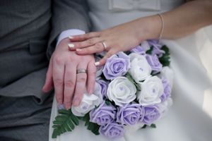 Wedding rings displayed on purple and white rose bouquet.