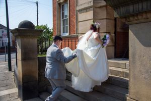 Wedding couple ascending stone steps outside brick building.