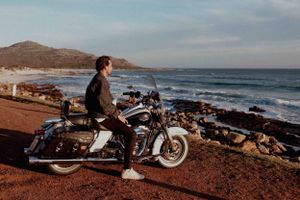 A motorcycle parked on a coastal road overlooking rocky shoreline at sunset.