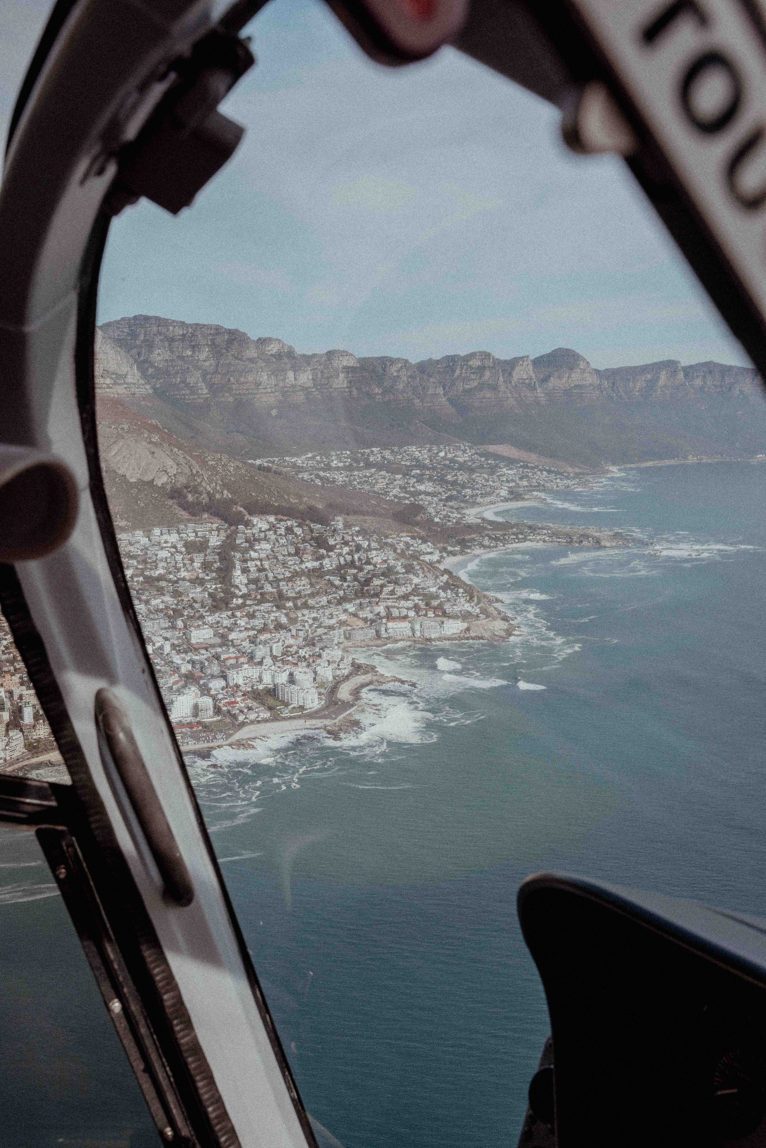 Aerial view of a rocky coastline and urban development seen through a helicopter window frame.