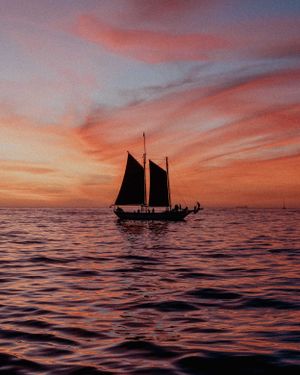 Silhouette of a traditional sailing ship against a vibrant orange and pink sunset over the ocean.