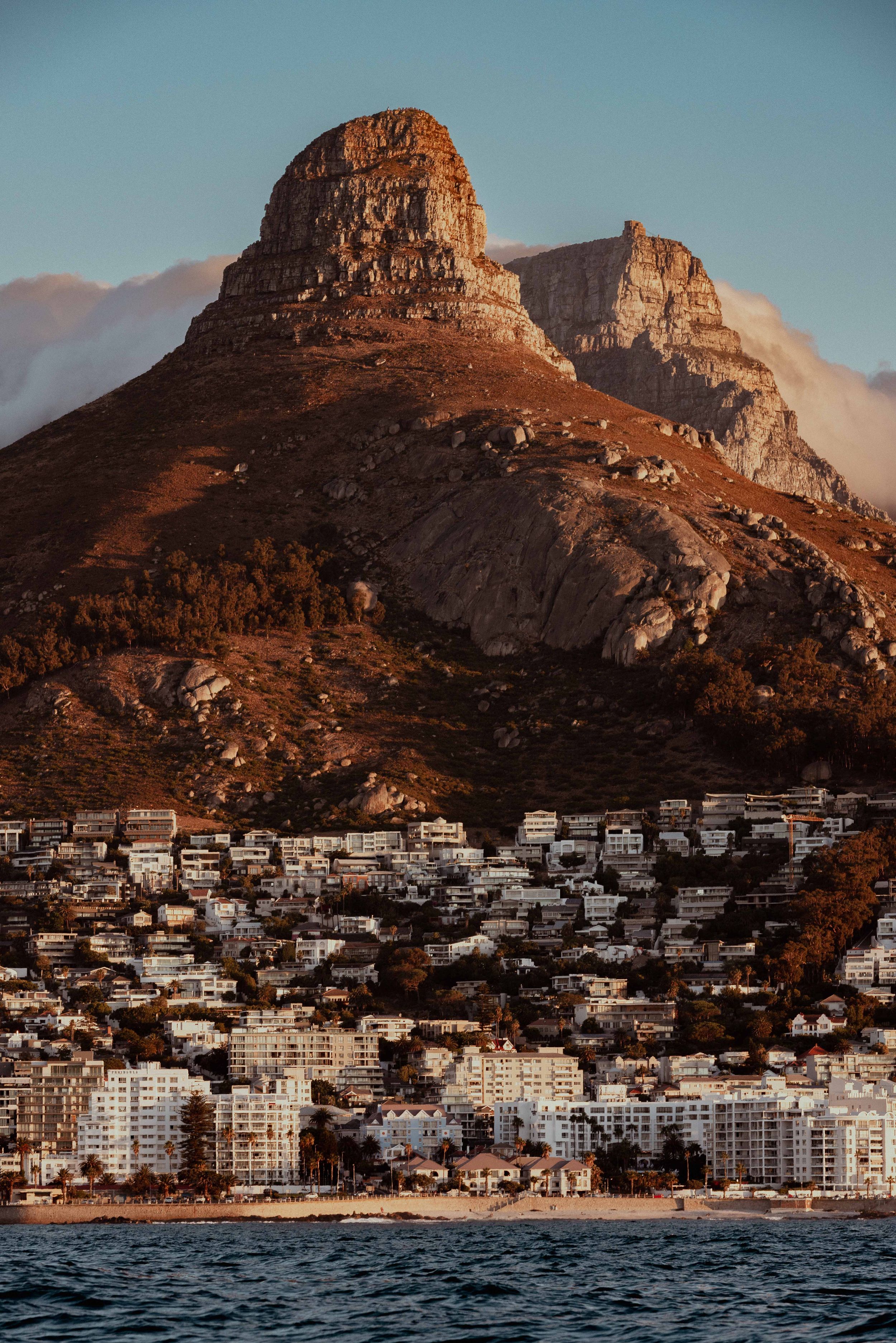 Dramatic view of Lion's Head mountain towering over coastal homes in Cape Town at sunset.