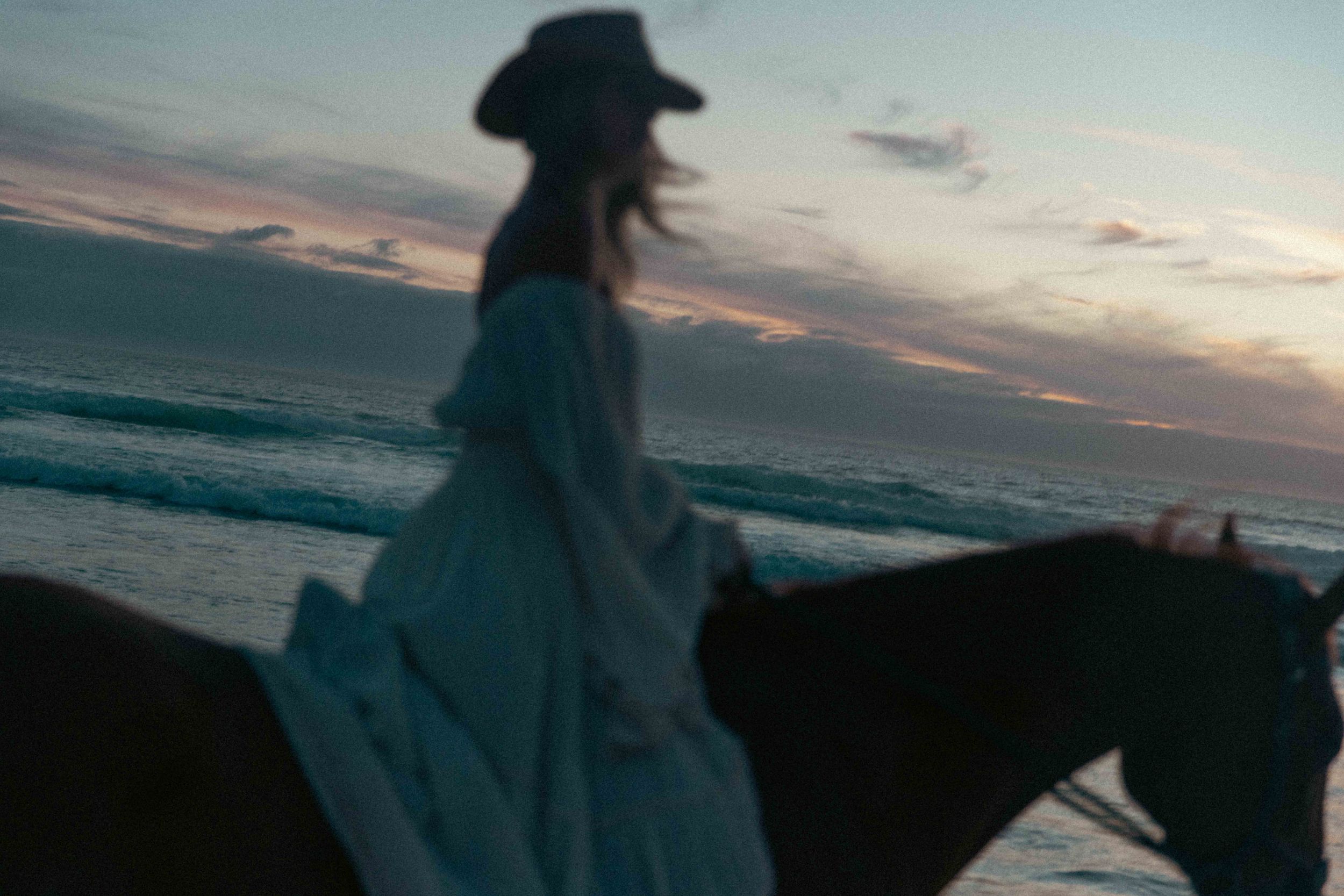 Silhouetted figure horseback riding along beach at sunset.