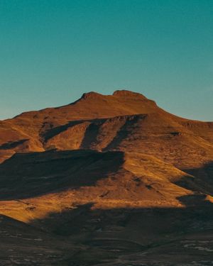 Rugged brown mountain peak against turquoise sky in dramatic lighting.