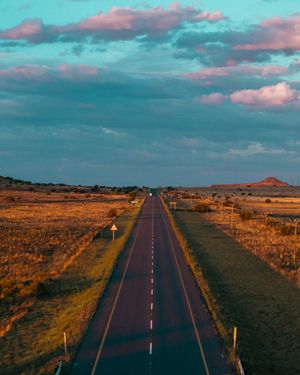 Empty highway stretching through desert landscape under turquoise and pink skies.