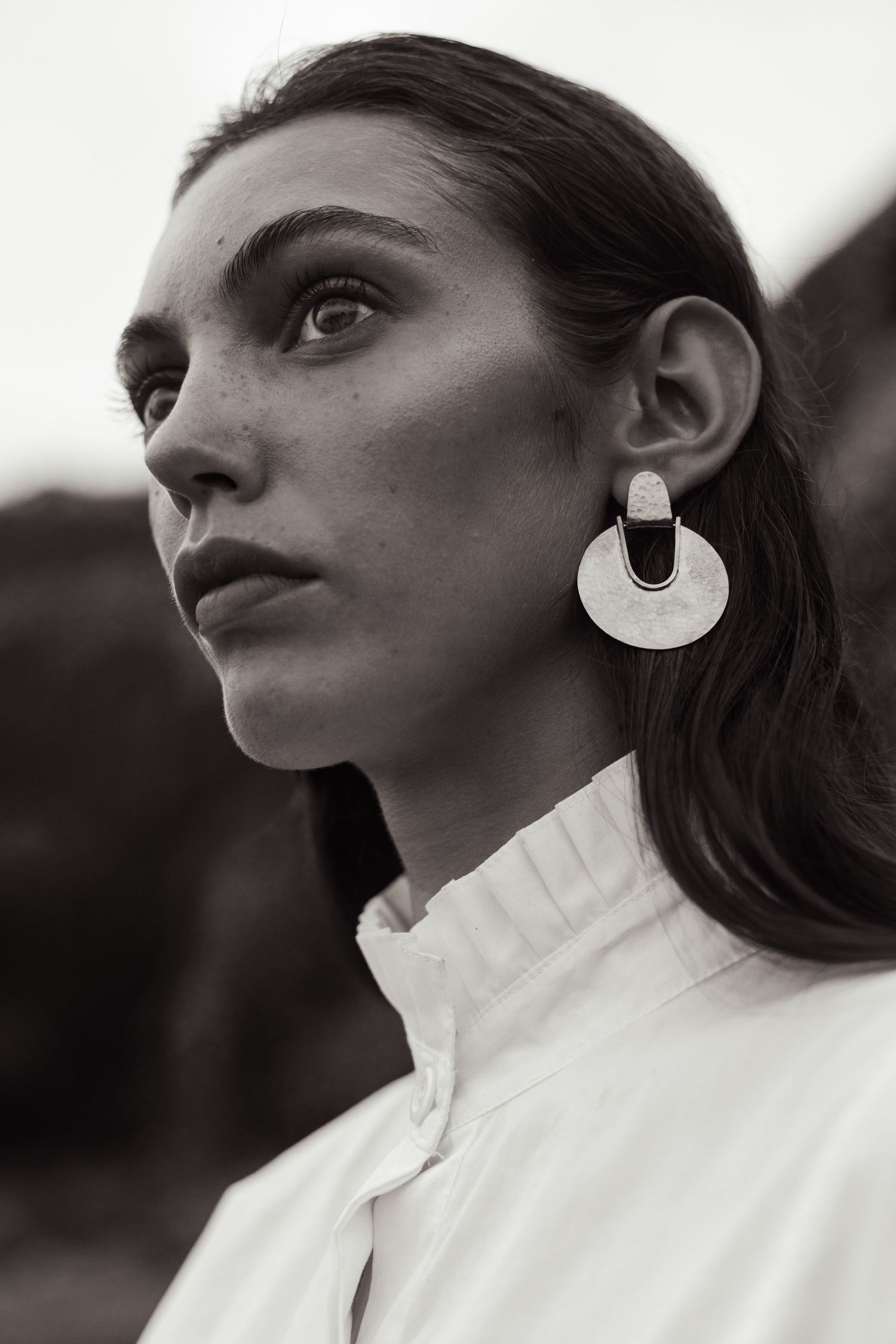 Close-up profile portrait with dramatic circular earring and white collar.