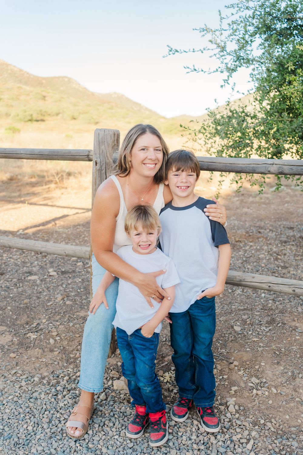 Family smiling together outdoors by wooden fence on sunny day in countryside setting.