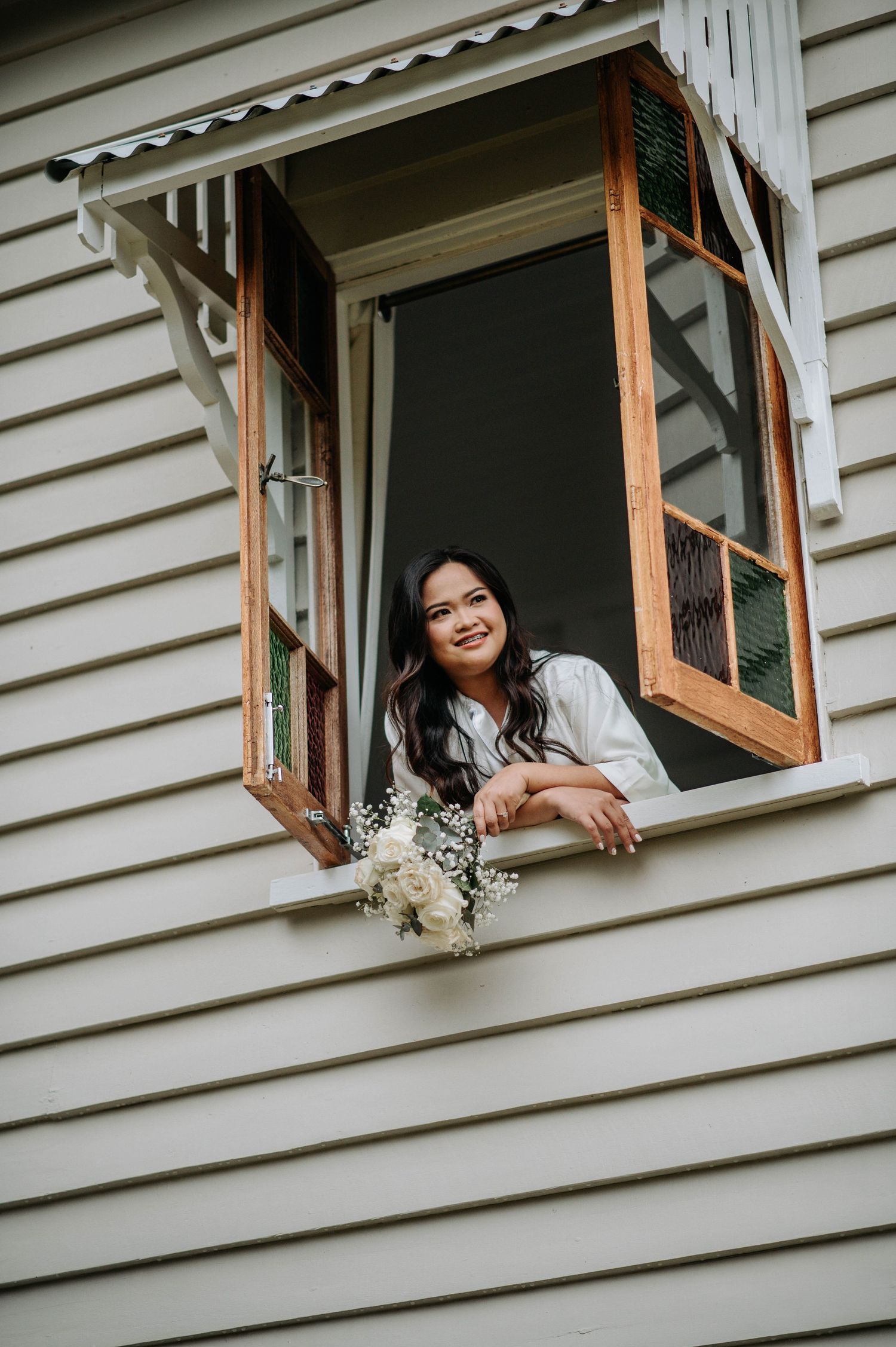 White clapboard house window frame with flowers on windowsill.
