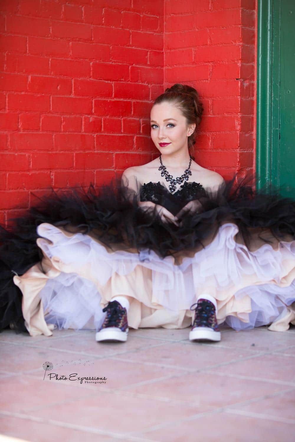 A black and white tulle dress contrasts against a bright red brick wall in an artistic portrait series.