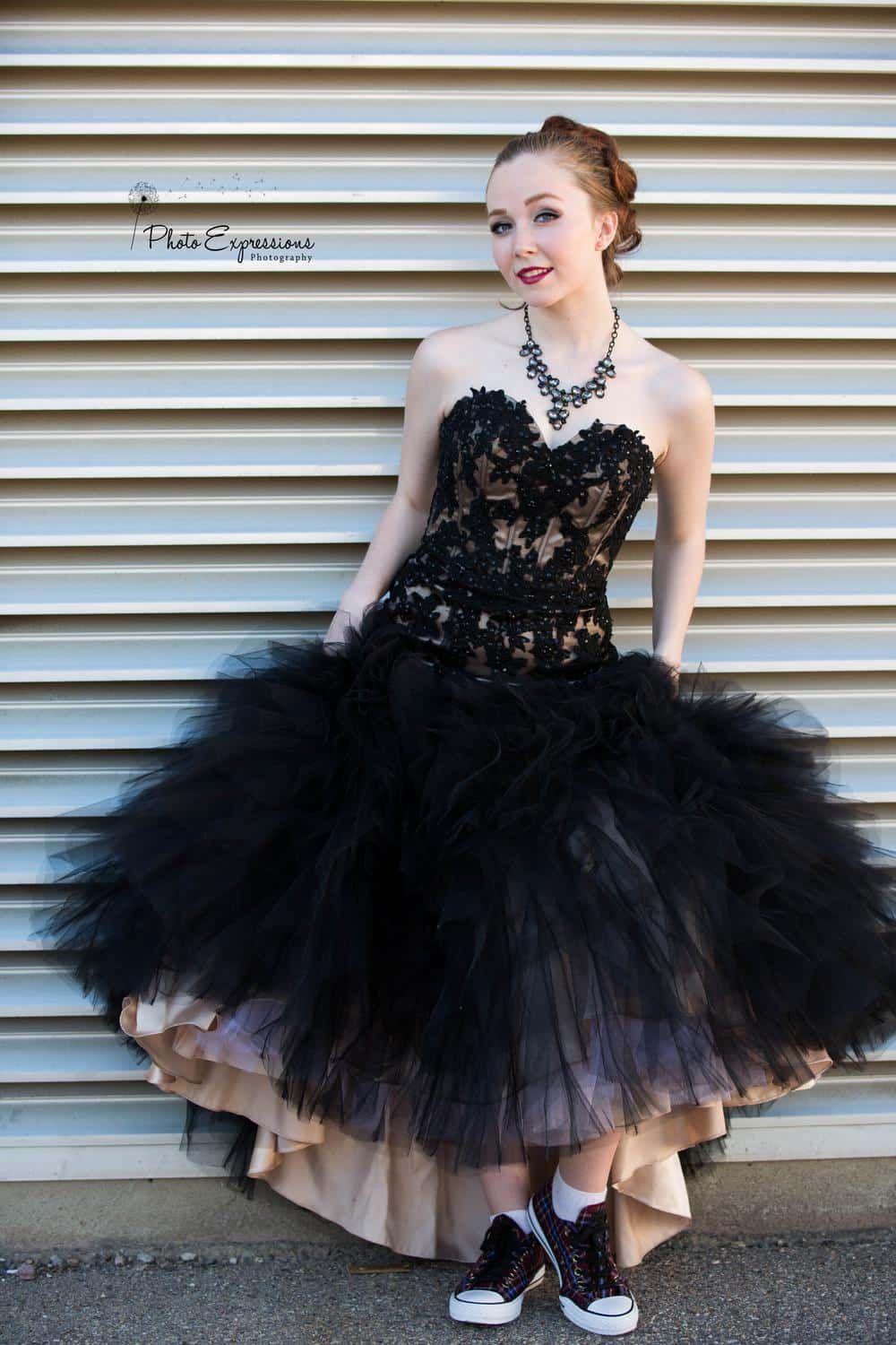 A dramatic black tulle gown with lace bodice is paired with casual sneakers in a fashion photoshoot against white panels.