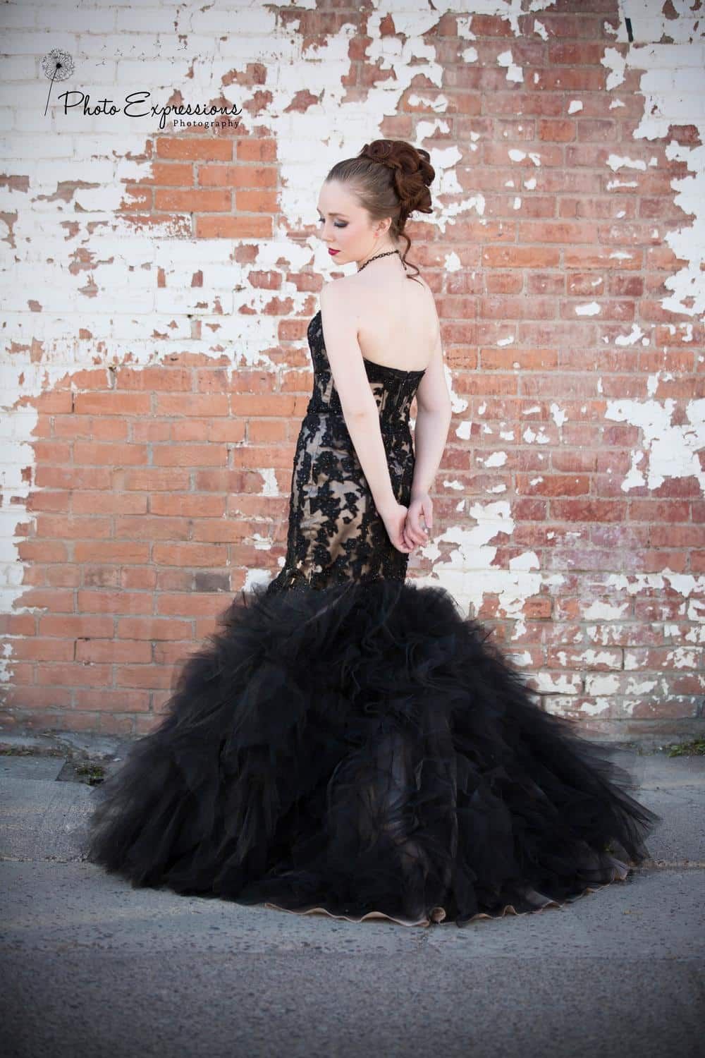 Back view of dramatic black lace and tulle evening gown against weathered brick wall.