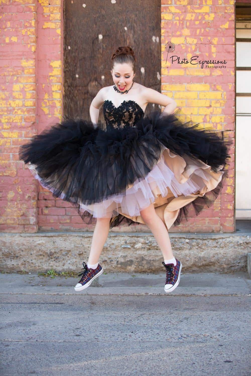 Playful fashion shot of black tulle dress with sneakers in mid-jump pose.