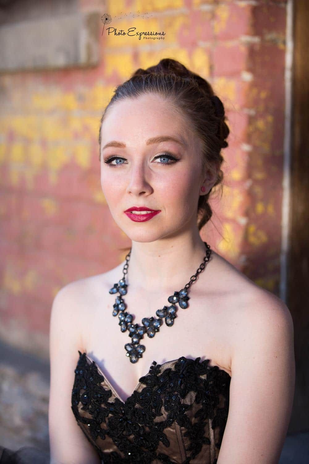 Elegant portrait with black statement necklace against weathered brick wall background.