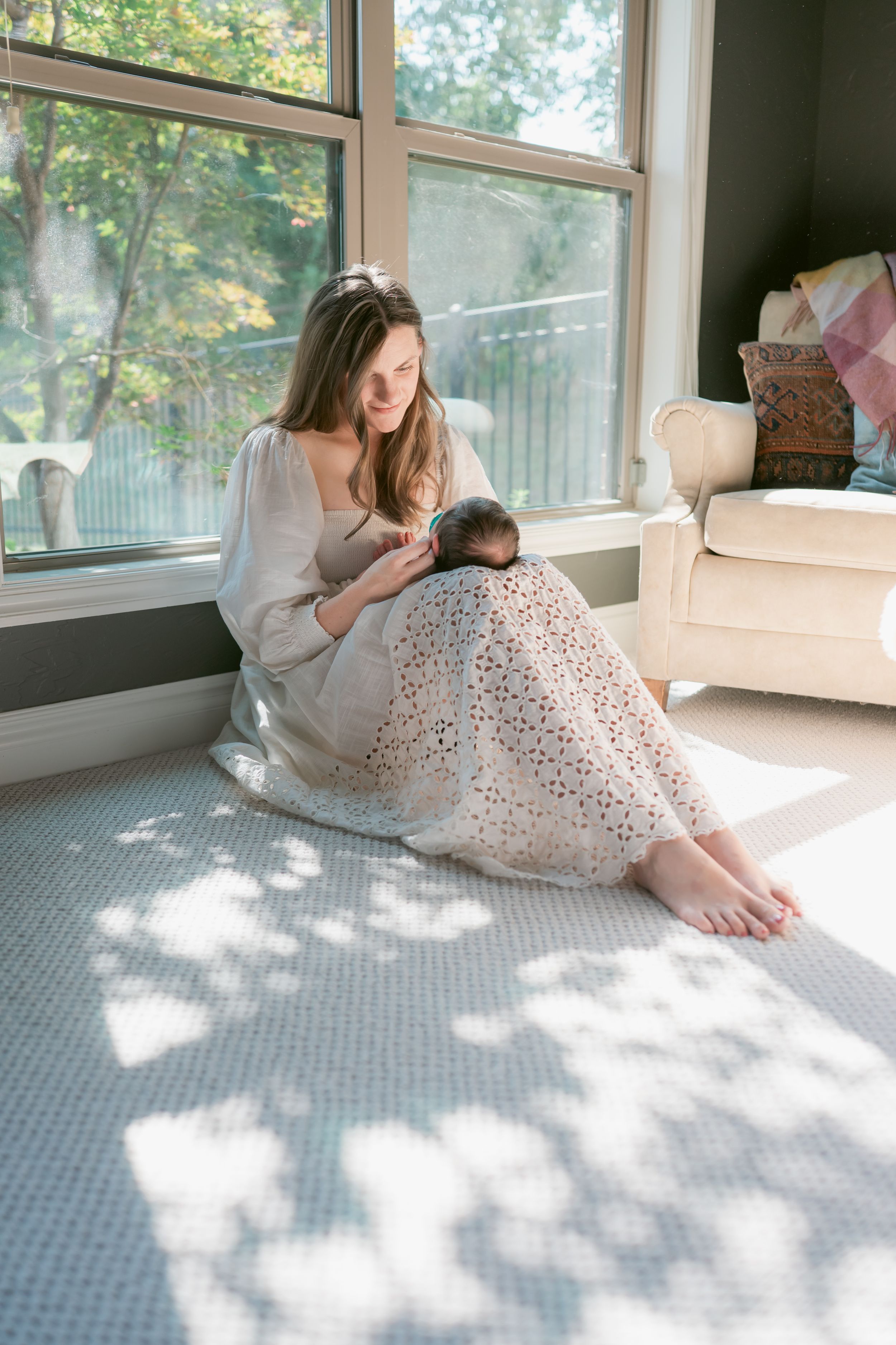 A luminous sunlit moment with a new mother reclining in a white dress shadows dance across the scene. For Edmond Newborn Photographer
