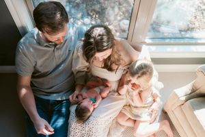 family sits in front of sun drenched window with newborn baby in lap for Edmond newborn photographer Lindsey K Brown photography