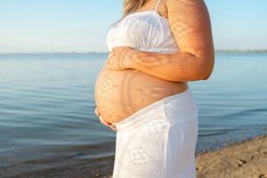 mother shows her pregnant belly with shadows on it in front of lake Hefner in OKC for Oklahoma City maternity photographer