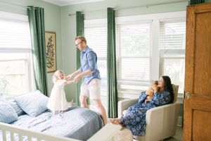family plays in bedroom while mother holds newborn baby for Oklahoma City newborn photographer
