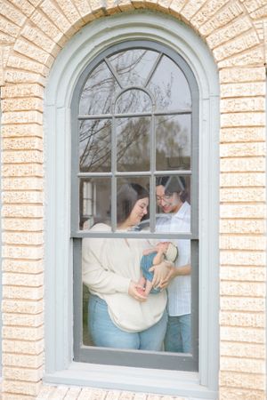 An arched window in Oklahoma City shows parents holding their newborn visible through the white-framed glass panes.