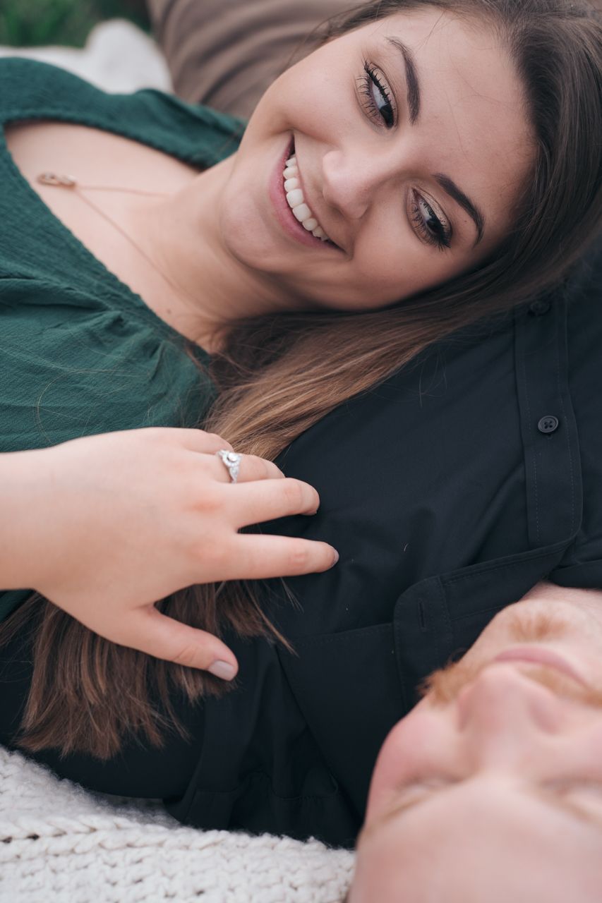 Person laying down wearing a green sweater showing off an engagement ring with a bright smile. Marion, Ohio