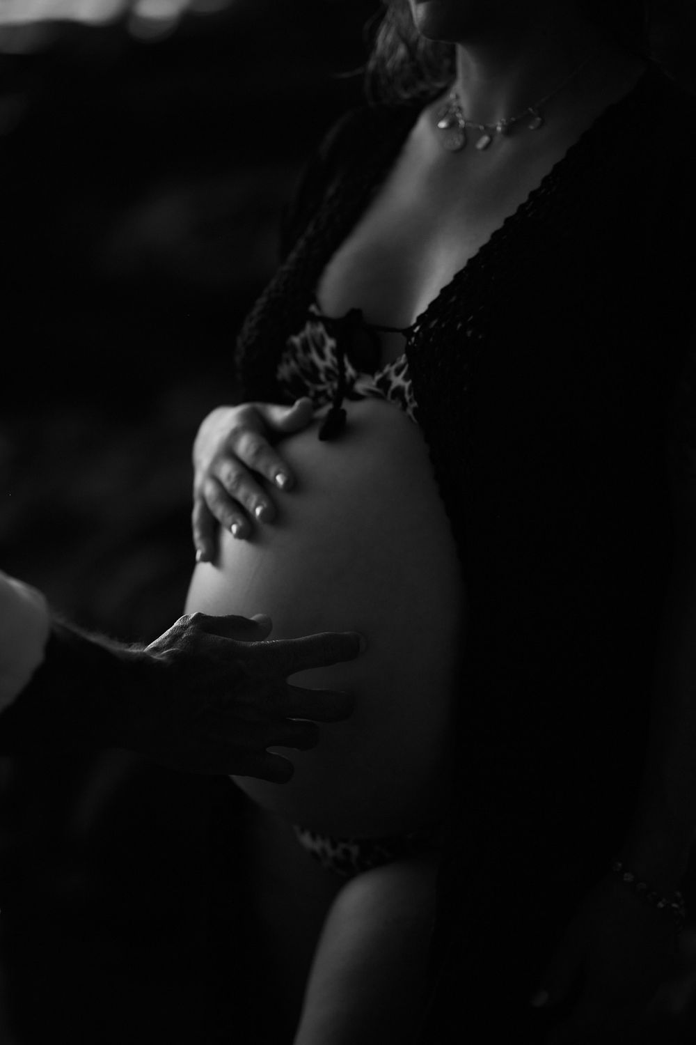 Black and white photo of a pregnant woman cradling her baby bump, wearing lingerie and a delicate necklace.