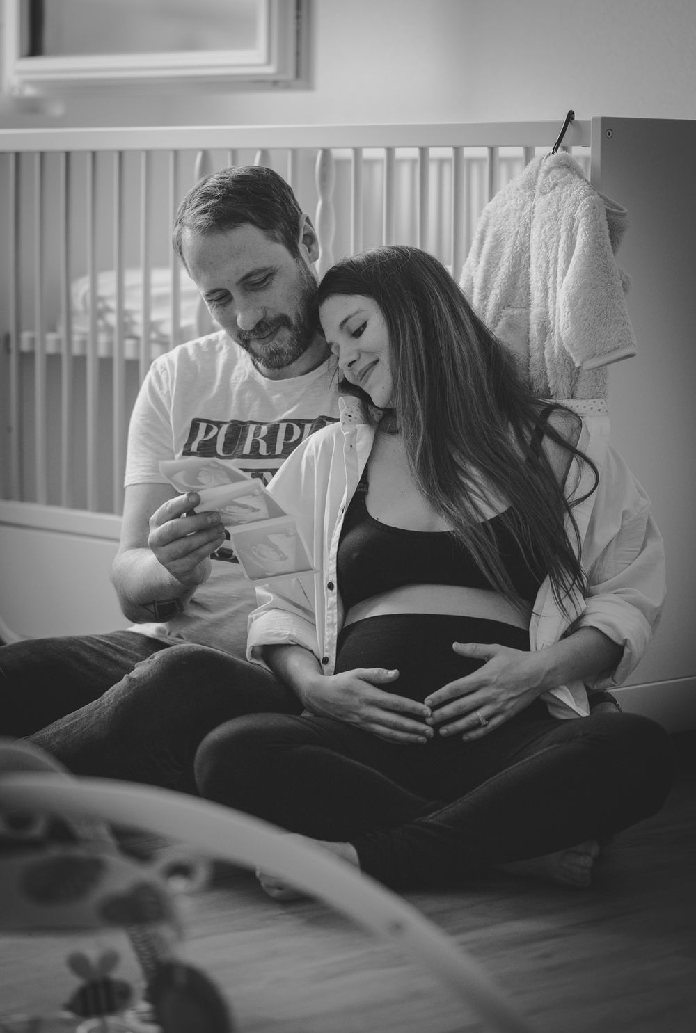 Black and white photo of couple looking at document in nursery setting.